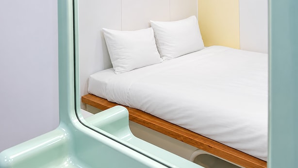 Ein Bett mit weißer Bettwäsche, einem Holzrahmen und einem weißen Kopfkissen.