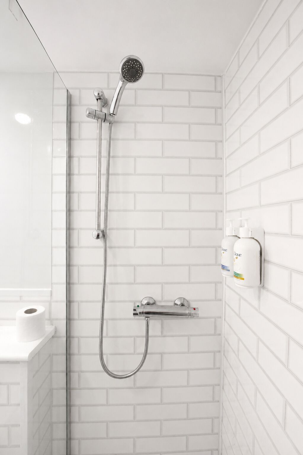 A shower with a handheld showerhead, a wall-mounted faucet, and a soap dispenser.