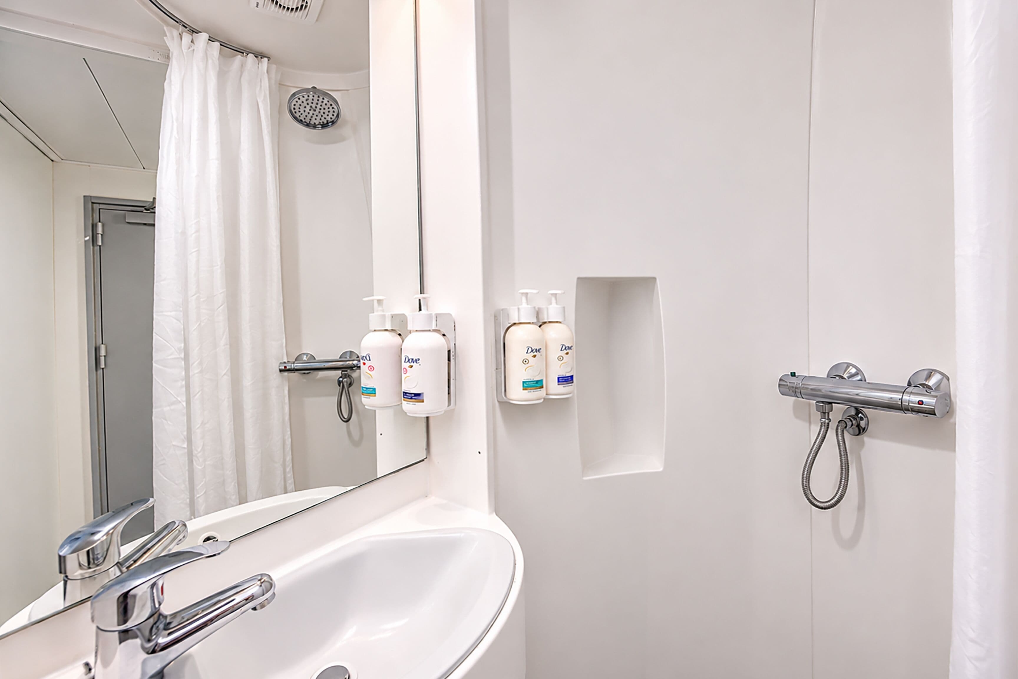 Et badeværelse med en hvid vask, et spejl, en bruser og toiletartikler på væggen.