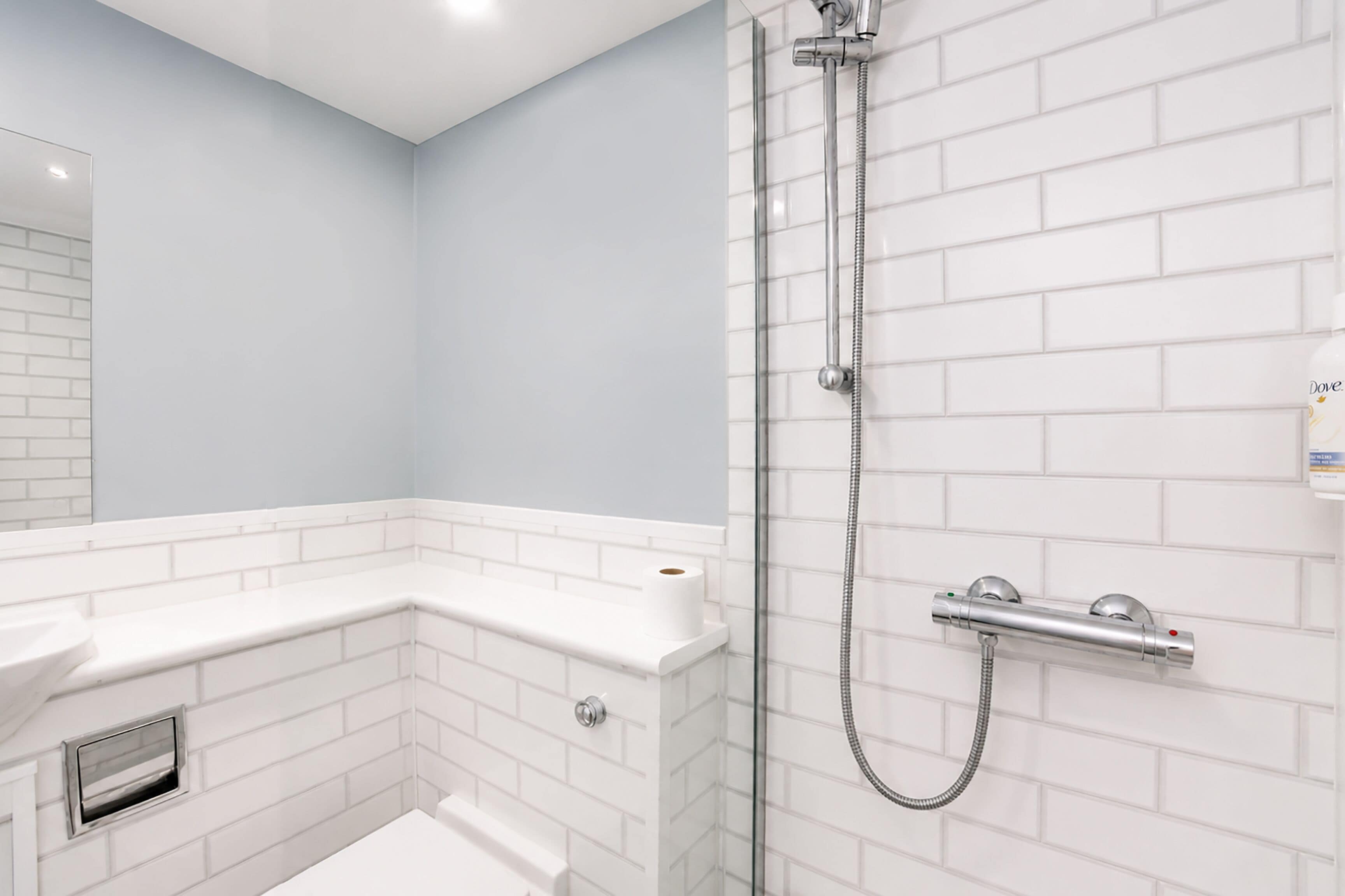 A bathroom with white subway tiles, a glass shower enclosure, a white sink, and a toilet.
