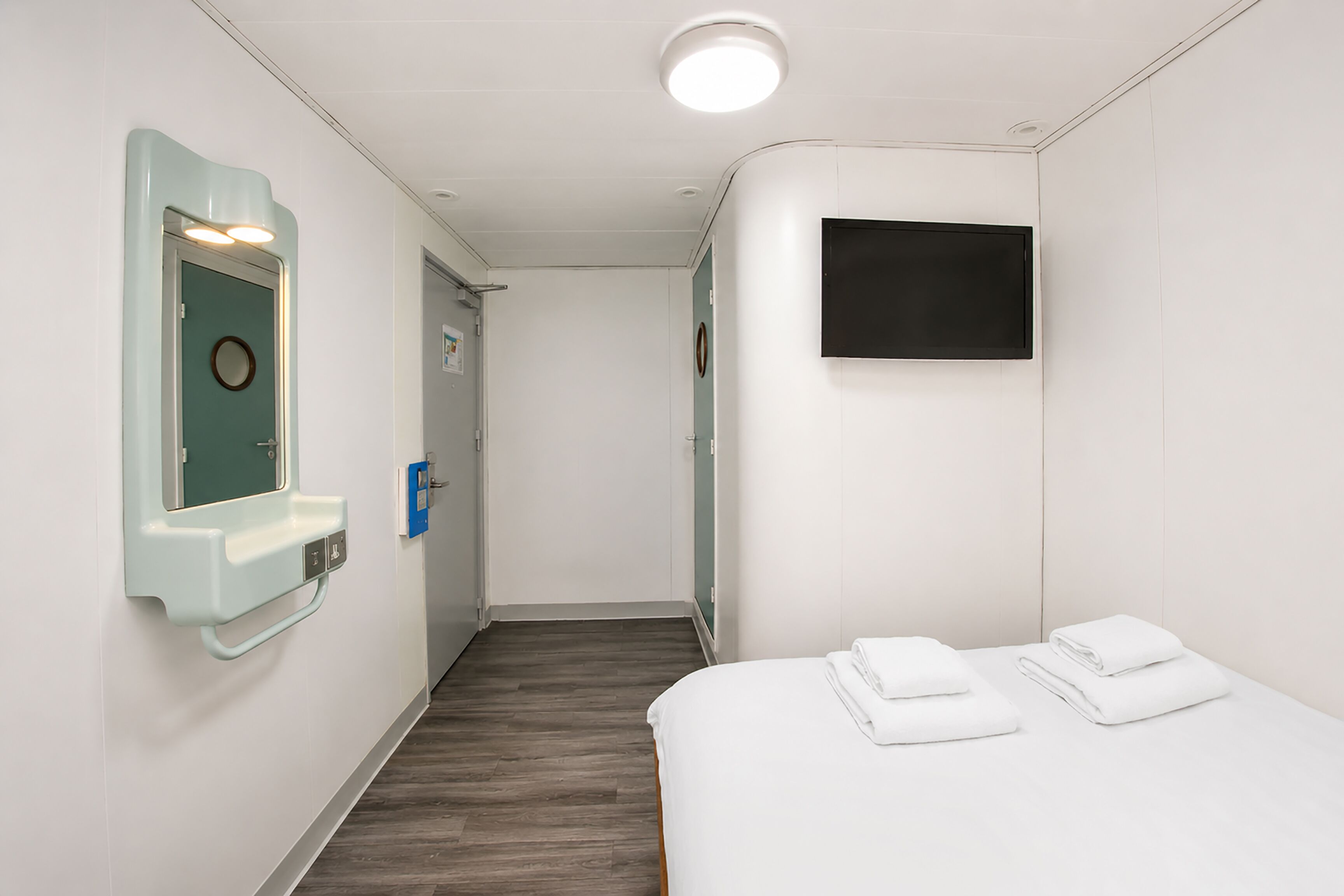 Hotellihuone, jossa on sänky, televisio, peili ja ovi.
