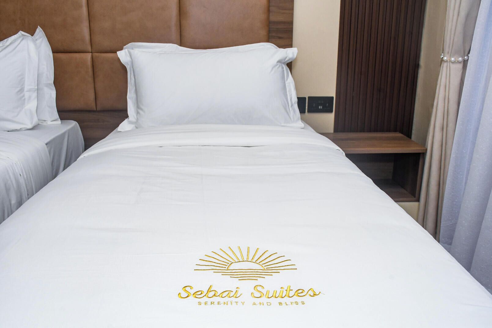 Una habitación de hotel con una cama, dos mesitas de noche, un cabecero de madera y un tocador.