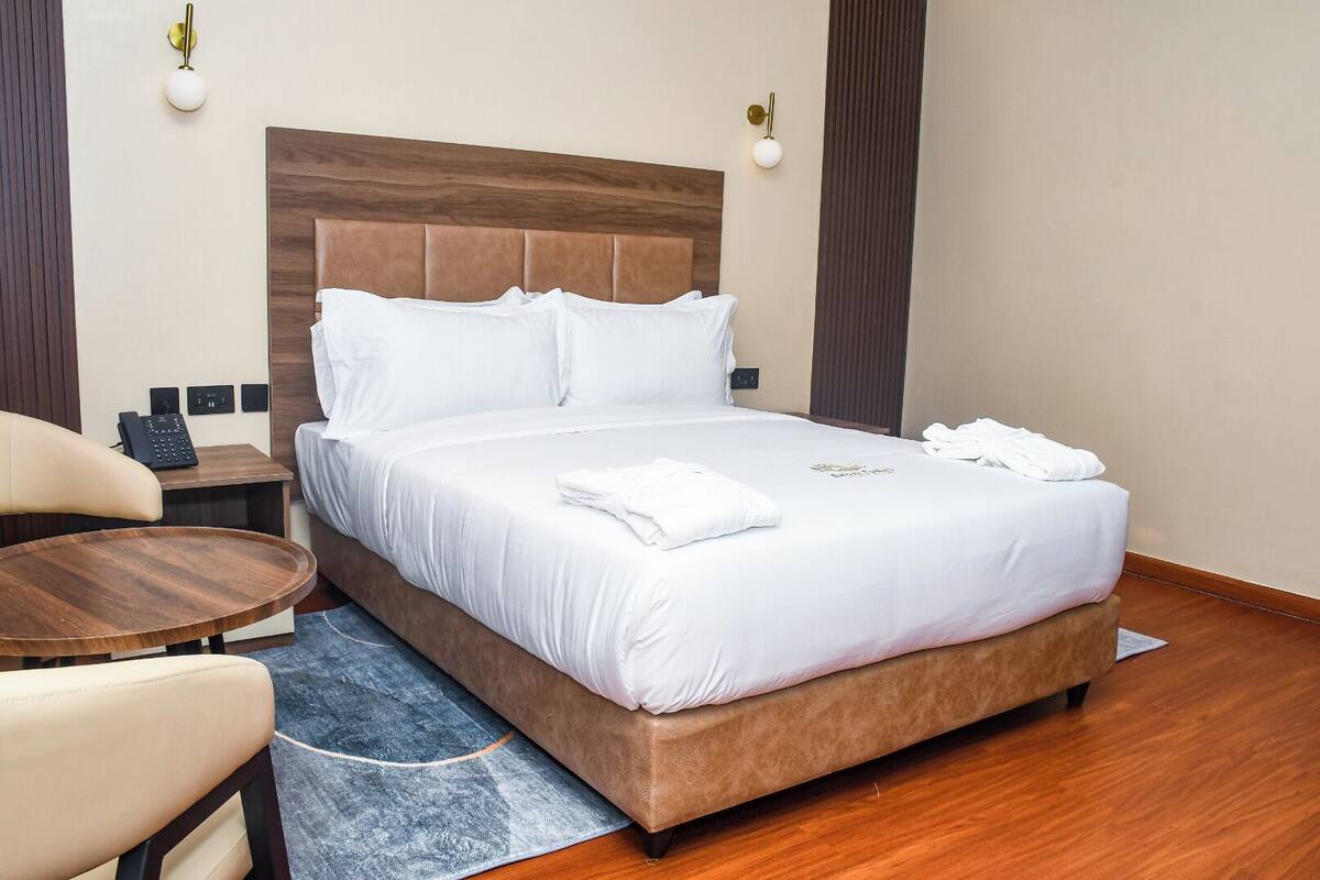 A hotel room with a bed, bedside table, chair, and a small desk with a telephone.