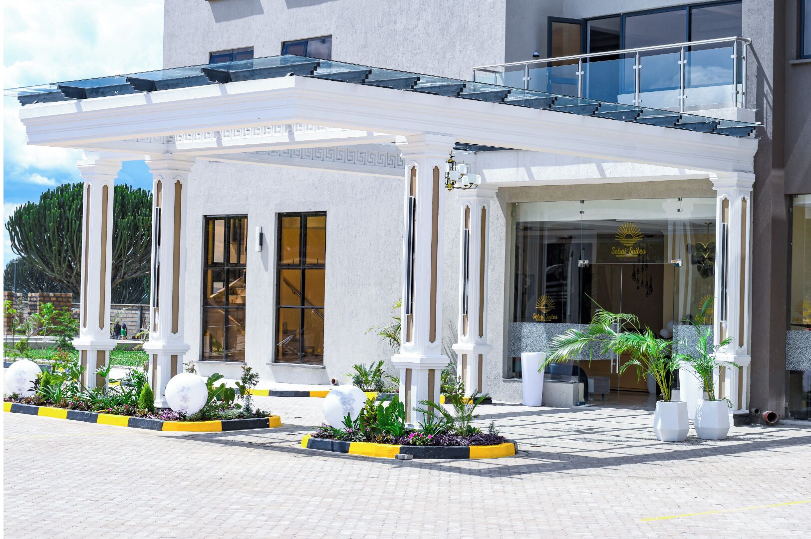 Ein Hotel Eingang mit überdachter Terrasse, großen Fenstern und Pflanzkübeln.