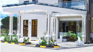 Ein Hotel Eingang mit überdachter Terrasse, großen Fenstern und Pflanzkübeln.