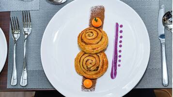 Ein Teller mit zwei spiralförmigen Gebäcken, einer kleinen orangen Frucht und einer violetten Soße.