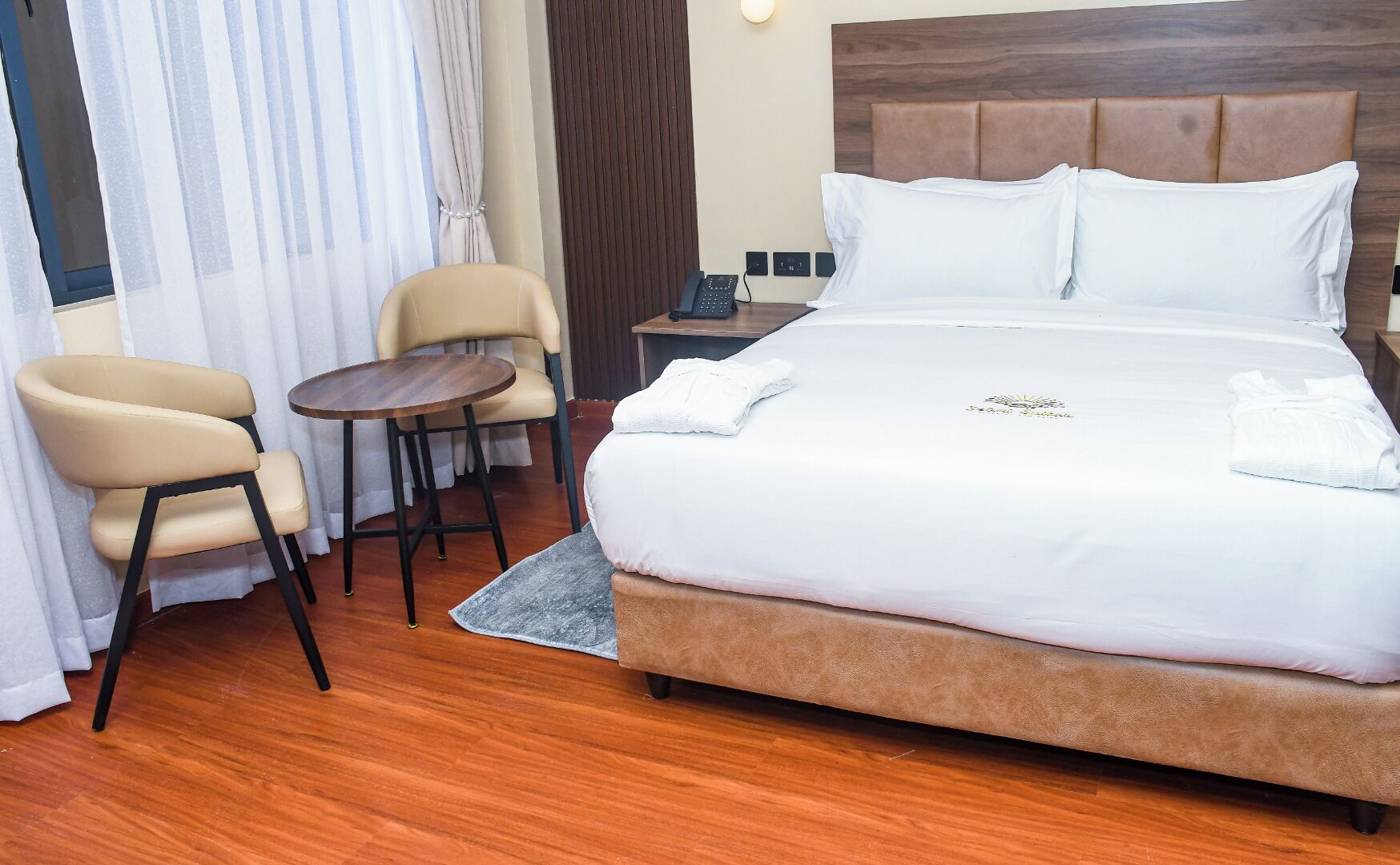 A hotel room with a large bed, a chair, a small table, and a nightstand.