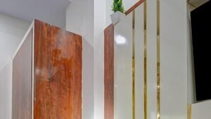 A room with a wooden wardrobe, a vanity with a mirror and lights, and a wooden chair. - Hotel Ambience (New Delhi)