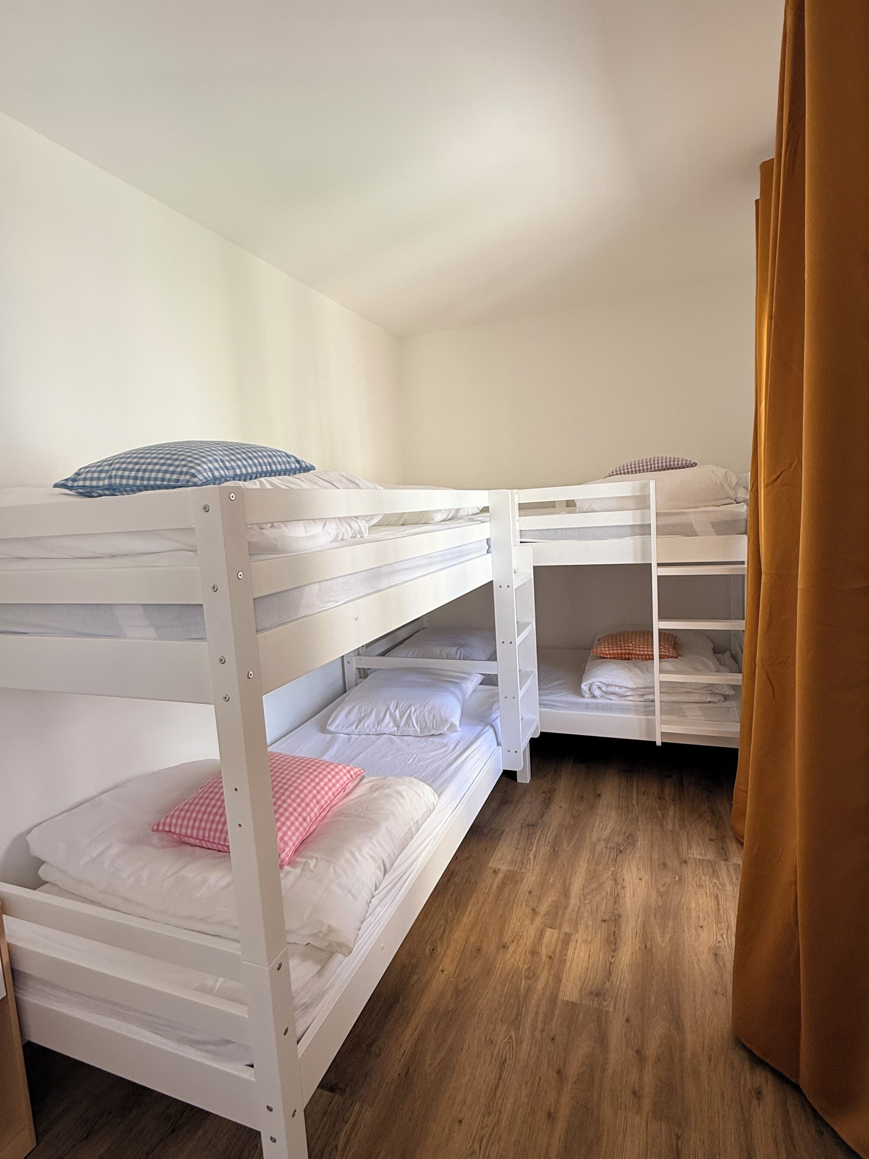 Een kamer met drie stapelbedden, houten vloeren en een bruin gordijn.