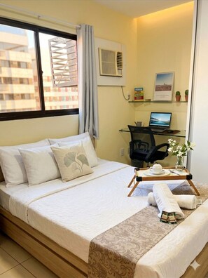 Une chambre d’hôtel avec un lit, un bureau avec un ordinateur portable, une chaise, une petite table avec une tasse et une soucoupe, et une fenêtre avec des stores.