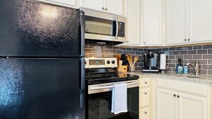 A kitchen with white cabinets, a black refrigerator, a microwave, a stove, and a coffee maker.