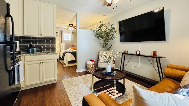 A modern living room with a sofa, coffee table, TV, and a kitchen area with cabinets and a refrigerator.