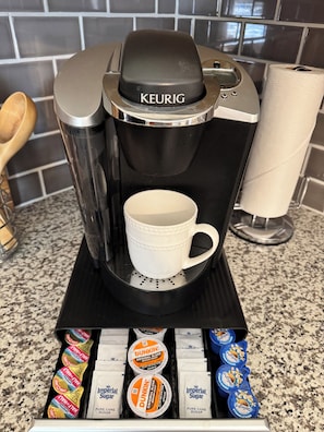 Une machine à café Keurig, une tasse blanche, un porte-essuie-tout et une boîte de dosettes de café Dunkin' Donuts.