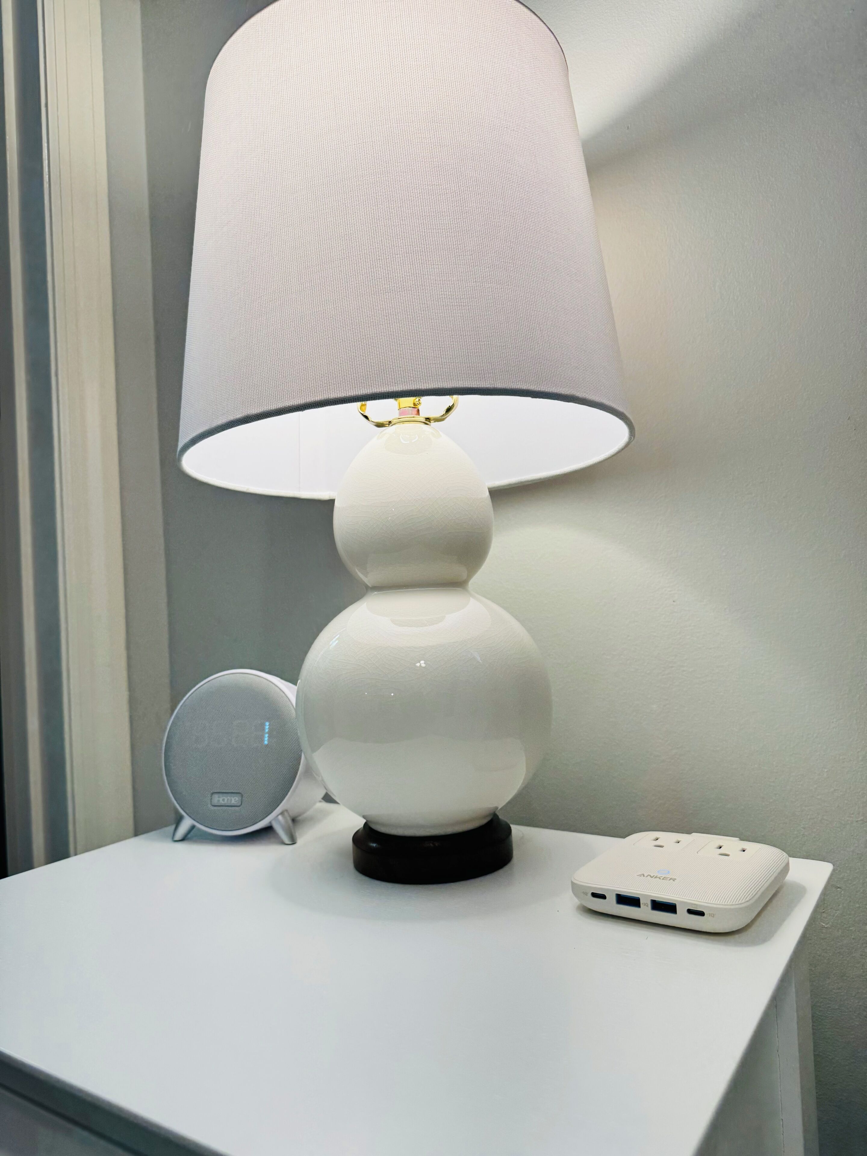 Une lampe blanche avec un pied rond et un abat-jour blanc, posée sur une table blanche.