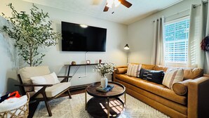 A living room with a sofa, a coffee table, a TV, a ceiling fan, and a large plant.