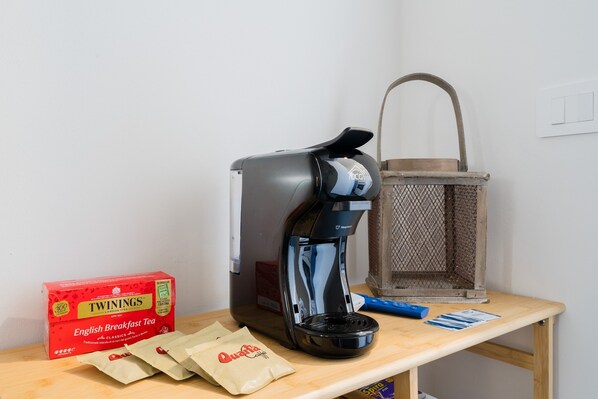 A coffee maker, Twinings English Breakfast Tea, and Quanta coffee bags on a wooden table.