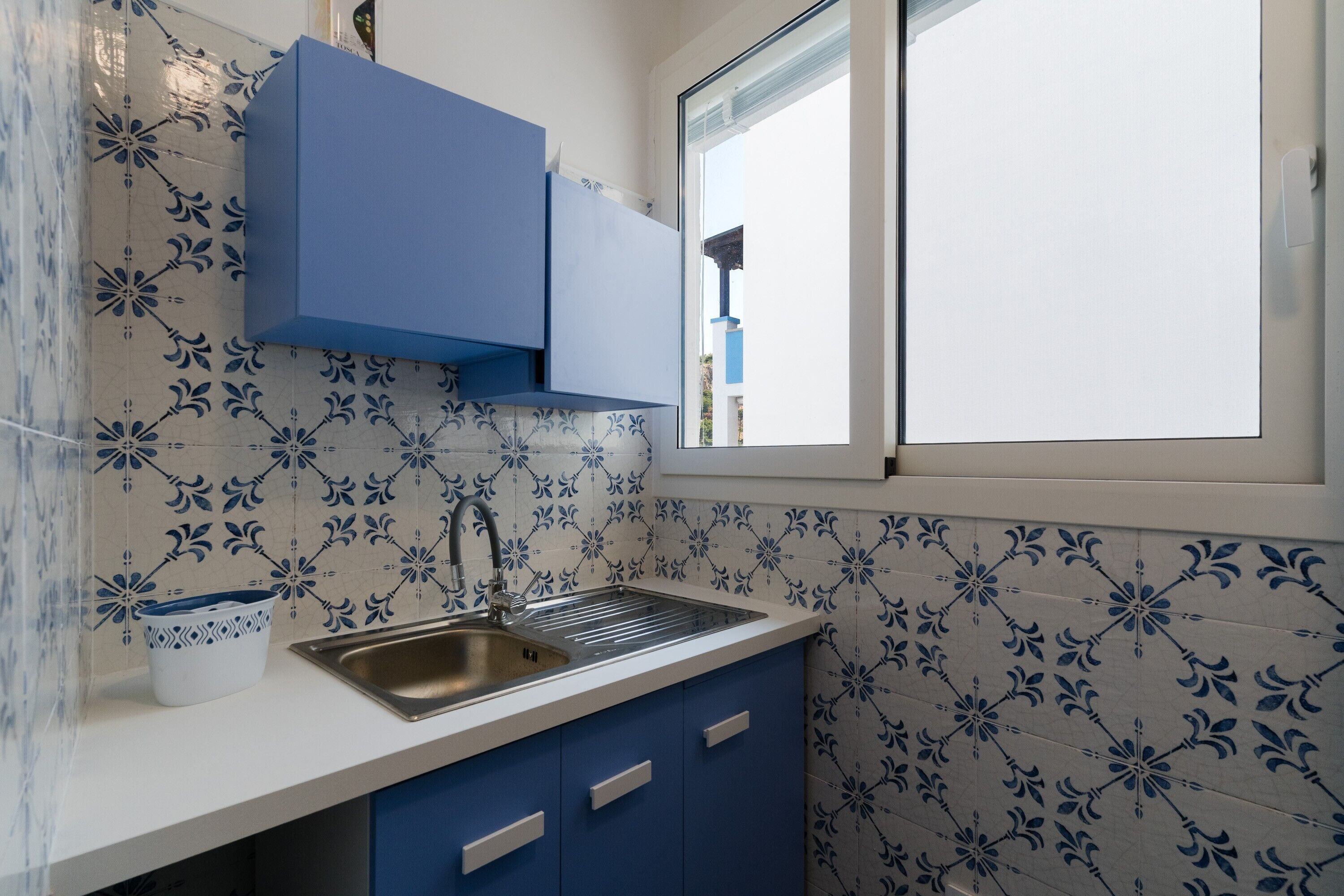 A kitchen with a sink, blue cabinets, and patterned tiles.