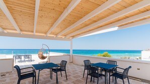 An outdoor patio with a wooden ceiling, stone floor, and a view of the sea.
