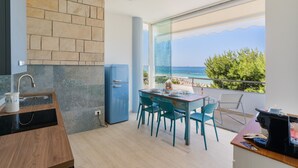 A modern kitchen with a view of the sea, a dining area with chairs, and a small table.