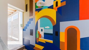 A hallway with a colorful abstract mural, a staircase, and a view of the outside.