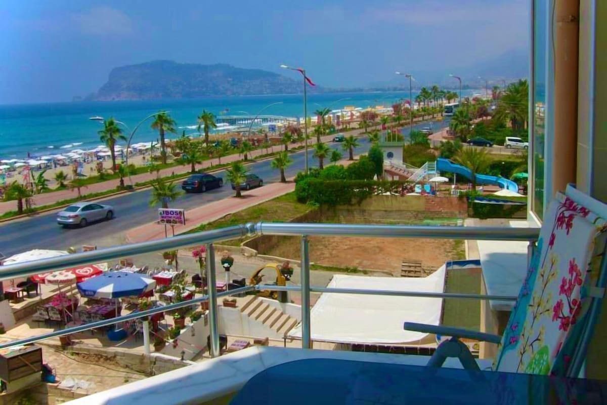 A balcony with a view of a beach, palm trees, and a road with cars.