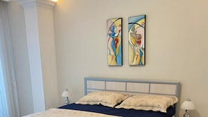 A bedroom with a bed, nightstands, a lamp, a star-patterned rug, and two abstract paintings on the wall. - ALANYAHOMES (Alanya)