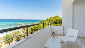 A balcony with a white table and chair, overlooking a beach and turquoise sea.