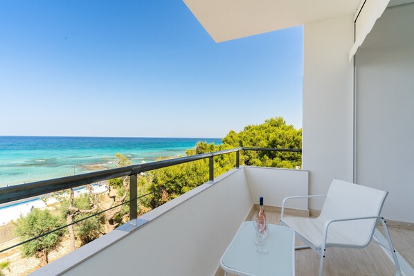 A balcony with a white table and chair, overlooking a beach and turquoise sea.