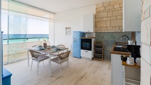 A modern kitchen with a blue refrigerator, a wooden dining table with chairs, and a view of the sea through large windows.