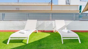 Two white sun loungers with towels on a green artificial grass lawn, against a white wall with a metal fence. - Luxury apartment near the cathedral of Seville (Sevilla)