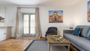 A living room with a sofa, a chair, a coffee table with magazines, and a painting of a building on the wall. - Luxury apartment near the cathedral of Seville (Sevilla)