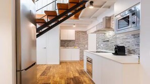 A modern kitchen with a wooden staircase, white cabinets, and a stone backsplash. - Luxury apartment near the cathedral of Seville (Sevilla)