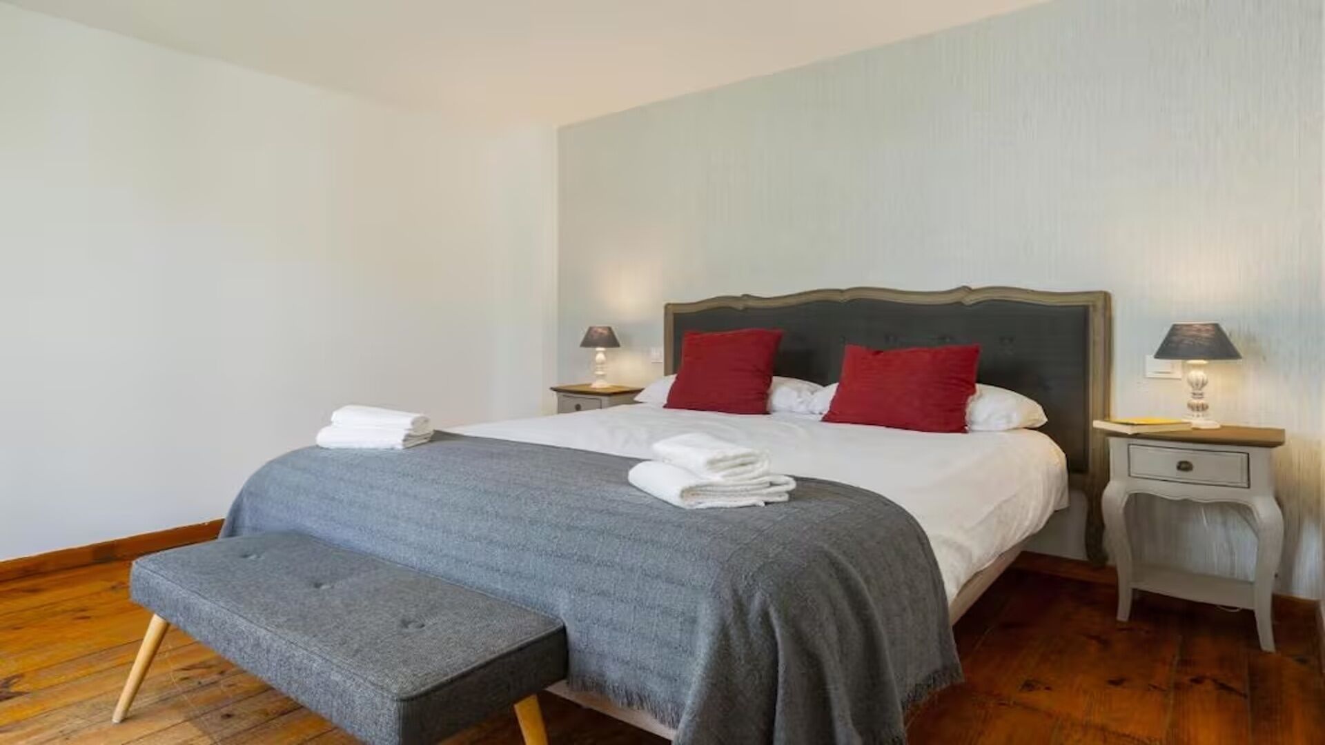 Un lit bien fait, avec des oreillers, une table de chevet avec une lampe et un banc au pied du lit.