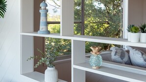 A white shelf with a lighthouse model, a vase with green foliage, and a decorative bottle. - Fliptide House - ocean views, spacious living and easy access to Kiama’s beaches (Kiama)