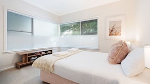 A bedroom with a bed, pillows, a bedside table, and a window with blinds. - Fliptide House - ocean views, spacious living and easy access to Kiama’s beaches (Kiama)