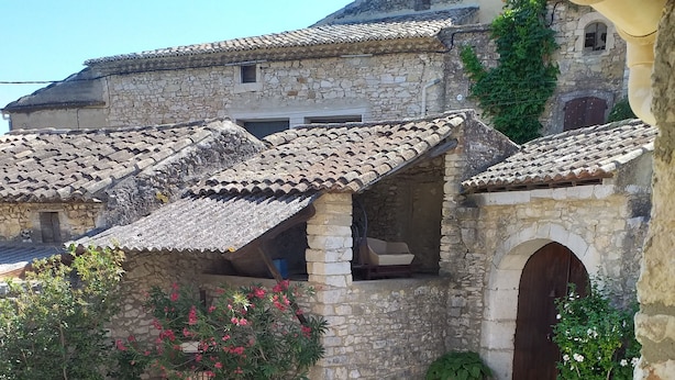 A stone building with a tiled roof, a small garden with flowering plants, and an arched doorway. - MAS PROVENCAL DE CARACTERE EN PIERRE. (Goudargues)
