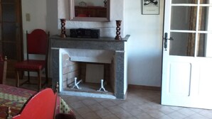 A room with a fireplace, a dining table with chairs, a door, and a wall-mounted lamp. - MAS PROVENCAL DE CARACTERE EN PIERRE. (Goudargues)