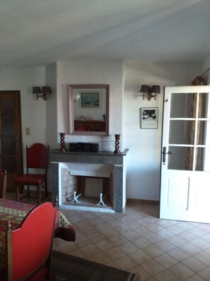 A room with a fireplace, a dining table with chairs, a door, and a wall-mounted lamp. - MAS PROVENCAL DE CARACTERE EN PIERRE. (Goudargues)