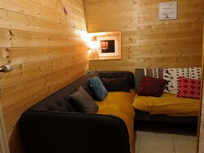A cozy cabin interior with a wooden wall, a sofa, a small table, and a lamp. - Old farmhouse (Châtelblanc)
