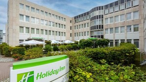 A Holiday Inn hotel with a courtyard, outdoor umbrellas, and a sign indicating the hotel's name. - Sunday One-bedroom Suite Twin Beds (Neu-Isenburg)