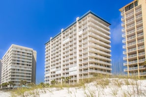 Un hotel frente a la playa con varios pisos, balcones y una playa arenosa en primer plano.