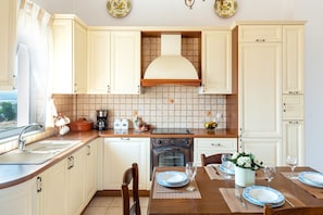 A kitchen with white cabinets, a tiled backsplash, a stove, and a dining area set with plates and glasses. - Villa Aeolos – Private Swim Spa, Sea View, Wi-Fi, Air Conditioning (Vigla)