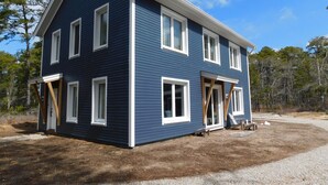 A two-story house with a gabled roof, white trim, and multiple windows. - Brand new GORGEOUS contemporary home (CS0054) (Wellfleet)