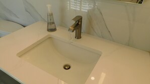 A bathroom sink with a modern faucet, a soap dispenser, and a marble wall in the background. - Brand new GORGEOUS contemporary home (CS0054) (Wellfleet)