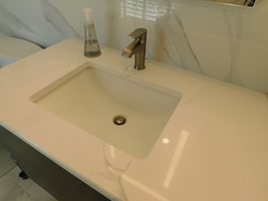 A bathroom sink with a modern faucet, a soap dispenser, and a marble wall in the background. - Brand new GORGEOUS contemporary home (CS0054) (Wellfleet)