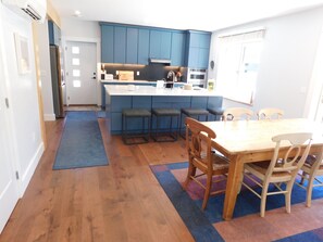A modern kitchen with blue cabinets, a central island, bar stools, and a dining table with chairs. - Brand new GORGEOUS contemporary home (CS0054) (Wellfleet)