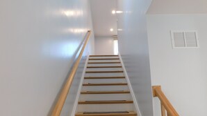 A staircase with wooden steps and a wooden handrail, leading to a landing with a white wall and a vent. - Brand new GORGEOUS contemporary home (CS0054) (Wellfleet)