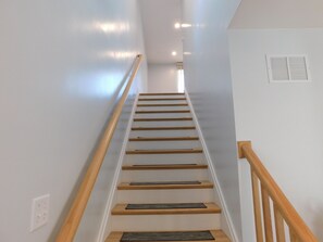 A staircase with wooden steps and a wooden handrail, leading to a landing with a white wall and a vent. - Brand new GORGEOUS contemporary home (CS0054) (Wellfleet)