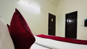 A hotel room with a bed, a red pillow, and two doors. - Hotel RS International (New Delhi)
