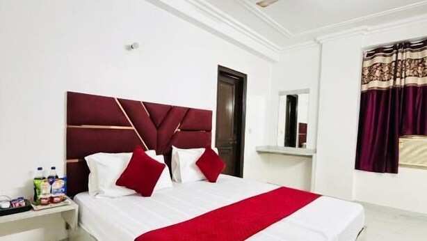 A hotel room with a bed, a nightstand, a ceiling fan, and a window with curtains. - Hotel RS International (New Delhi)